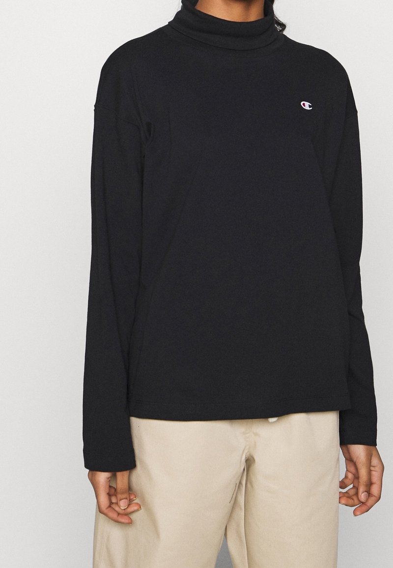 T-shirt noir à manches longues avec col roulé, fabriqué en tissu doux, comportant un petit logo sur la poitrine et une coupe décontractée avec un ourlet droit.