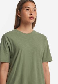 Kortärmad tröja med rund hals i olivgrönt tyg med en mjuk textur. Har en avslappnad passform och sömlös design vid axlarna.