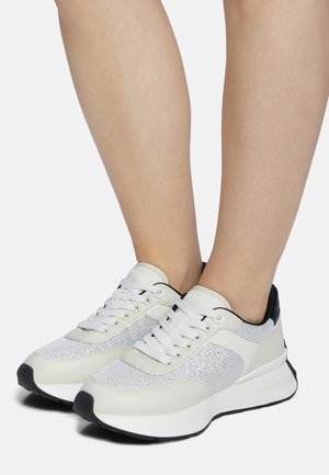 White athletic shoes showcasing a mesh upper, smooth leather accents, round toe, and a thick white sole with a black rubber outsole.