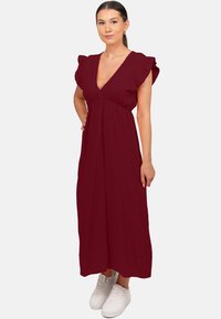 Abito maxi borgogna con scollo a V, maniche corte a volant e vita arricciata. Indossato con sneakers bianche, caratterizzato da un tessuto testurizzato.