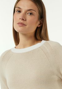 Beige gestrickter Pullover mit einem weißen Rippkragen. Verfügt über ein strukturiertes Muster und Raglanärmel, was eine lockere Passform schafft.