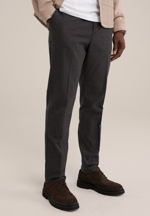 Pantaloni grigi scuri su misura con un motivo sottile, taglio dritto e tasche. Abbinati a scarpe in suede marroni e a una giacca leggera.