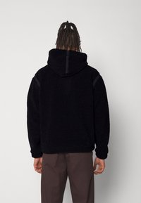 Schwarzer Fleece-Hoodie mit strukturiertem Finish, langen Ärmeln und Kordelzugkapuze. Mit Kontrastpaneelen an den Schultern.