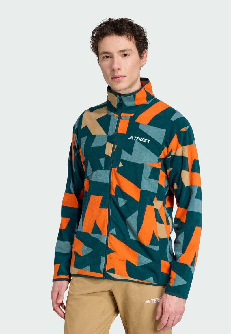 Fleecejacke mit geometrischen Mustern in Grün, Orange und Grau. Voller Reißverschluss, hoher Kragen, mit Logo auf der linken Brust. Weiche Textur.