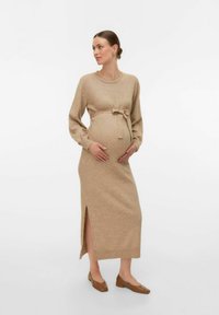 Abito premaman in morbido knit beige, con maniche lunghe, vita con laccetto e uno spacco laterale, abbinato a scarpe basse marroni.