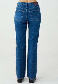 Niebieskie jeansy z denimu o prostych nogawkach, wysokim stanie, widocznymi tylnymi kieszeniami oraz metką marki z tyłu. Teksturowany, wytrzymały materiał.