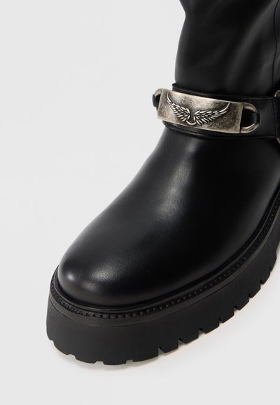 Schwarze Leder-Stiefelette mit runder Zehe, texturierter Oberfläche und einem metallisch-silbernen Schnalle-Detail mit Flügel-Design. Grobe Laufsohle.
