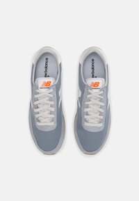 Sneakers azzurri chiari con tomaia in rete e suede, lacci bianchi e suola in gomma. Presentano un logo New Balance arancione.