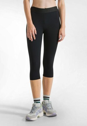 Leggings neri fino al ginocchio con una texture liscia e una fascia larga in vita, abbinati a scarpe da ginnastica grigie e calze a righe.