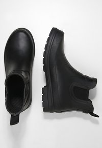 Botas de tobillo negras de goma, con un forro interior texturizado, paneles laterales elásticos y una suela gruesa y con patrón para agarre.