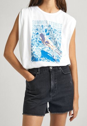 Chemise sans manches en coton blanc avec un graphique "HISTOIRES D'ÉTÉ", présentant de l'eau de piscine bleue. Assortie à un short en denim foncé avec un ourlet effiloché.
