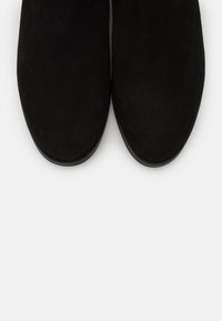 Bottines en daim noir avec un bout rond et une texture lisse, présentant un design minimaliste et un éclat subtil.