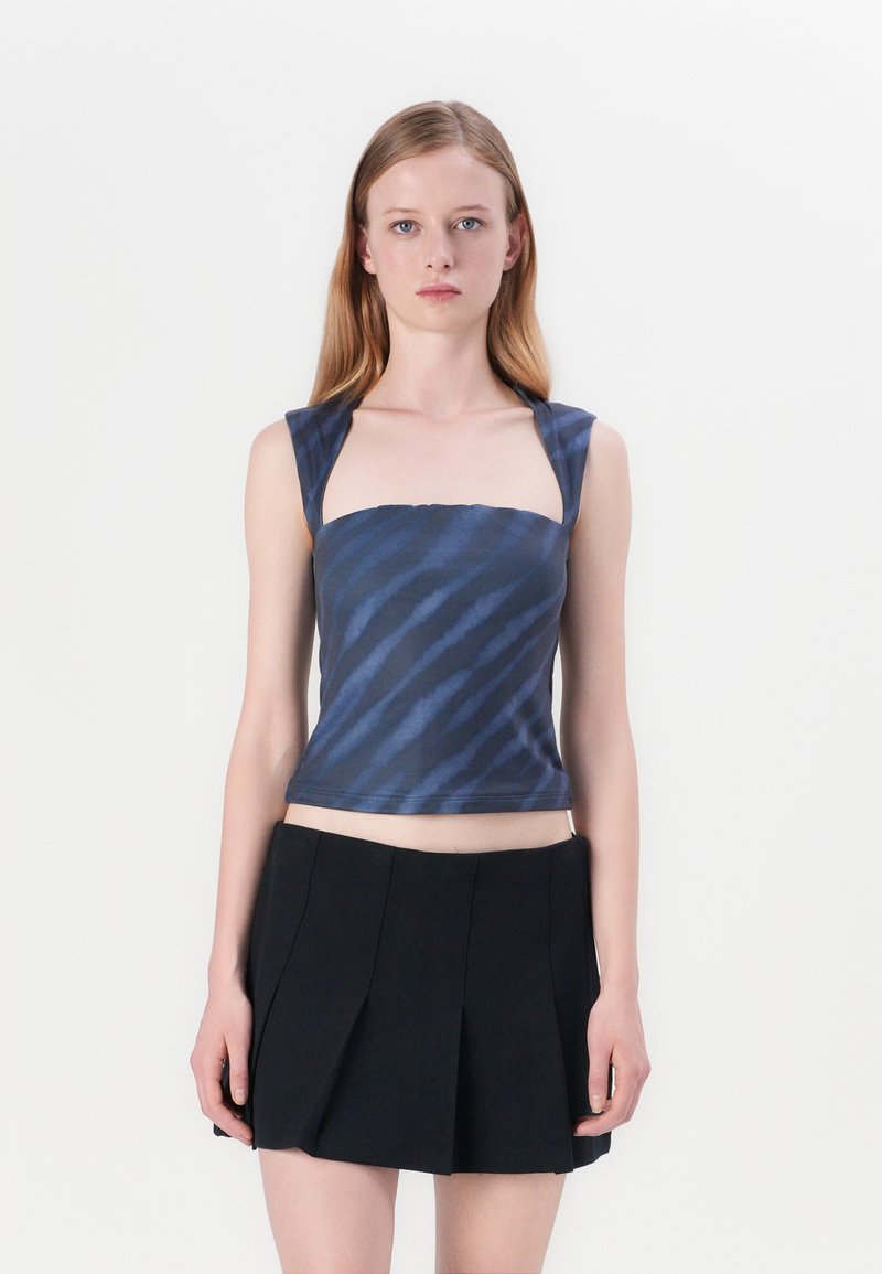 Kék és sötétkék mintás crop top, négyzet alakú nyakkivágással és széles pántokkal, fekete, pliszírozott mini szoknyával párosítva. Simább anyag textúra.