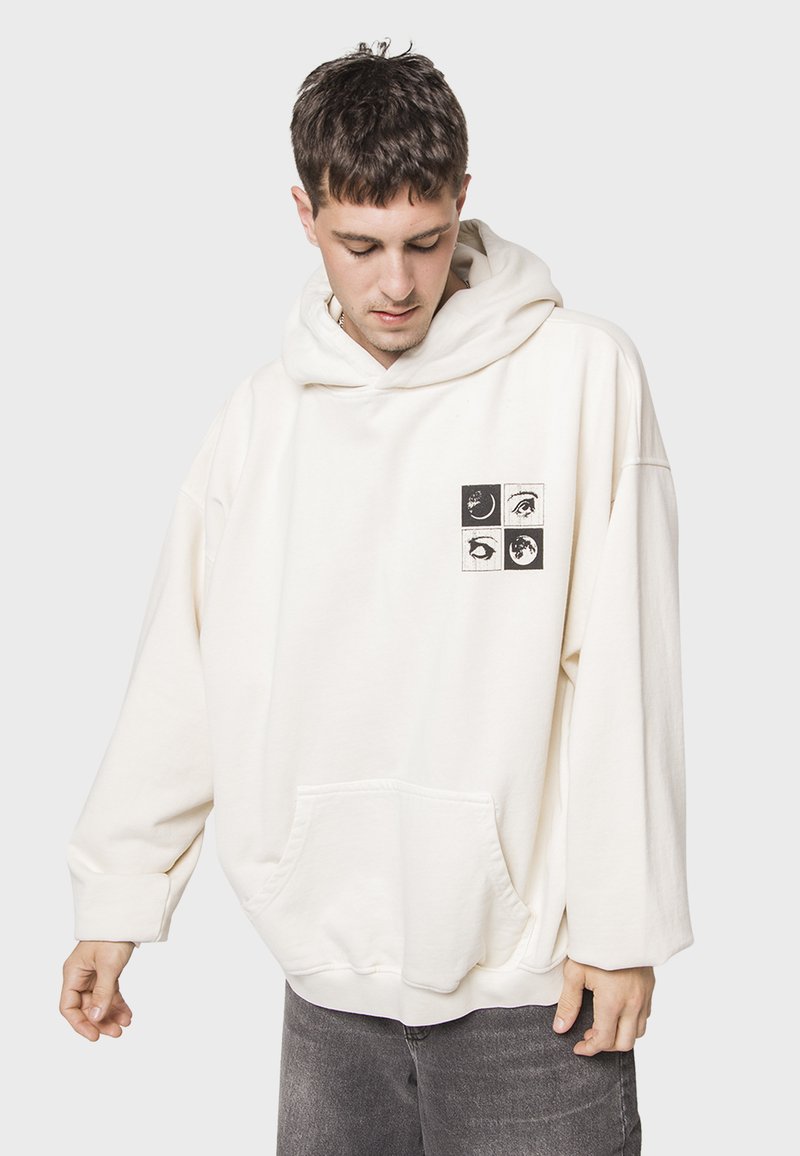 Sudadera de gran tamaño color crema con un bolsillo tipo canguro, que presenta un gráfico impreso con cuatro imágenes cuadradas negras en el pecho.