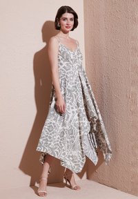 Maxi jurk in lichtgrijs met abstracte witte patronen, met een aansluitende lijfje, dunne bandjes en een asymmetrische zoom. Glad stof.