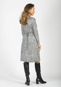 Harmaa kuviollinen mekko, jossa on pitkät hihat, vyötäröä korostava yksityiskohta ja polven mittainen helma, yhdistettynä mustiin polviasusteisiin saappaisiin. Sileä kankaan todella.