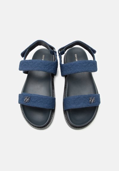 Ανδρικά σανδάλια σε ναυτικό μπλε χρώμα με δύο ρυθμιζόμενα υφασμάτινα λουριά και μαύρα μαξιλαράκια στα πέλματα, φαίνονται από πάνω σε λευκό φόντο.