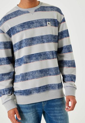 Man draagt een grijze sweatshirt met lange mouwen met brede, gestructureerde blauwe horizontale strepen en een klein logopatch op de borst.