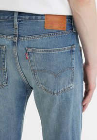 Světle modré džíny z denimu s klasickým pětipocket designem. Mají koženou nášivku na pase a červenou tabulku na zadní kapse.