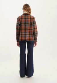 Veste en laine à carreaux dans des tons rouille, bleu et jaune, avec un col et des manches à boutons, assortie à un jean en denim foncé évasé.