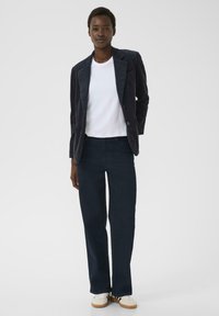 Dunkelblazer aus Cord in Navy über einem weißen T-Shirt, kombiniert mit dunkelblauen Hosen und weißen Sneakers. Weiche Textur mit strukturiertem Design.