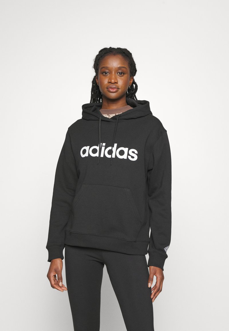 Črna kapuca s puloverjem z velikim belim logotipom "adidas", sprednjim žepom in rebrastimi manšeti. Uporabljena z črnimi leginami. Gladka tekstura tkanine.