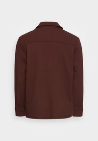 Braunes langärmliges Poloshirt mit strukturiertem Stoff, klassischem Kragen und dezenten Nähten an den Schultern und an den Bündchen.