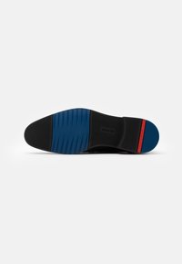 Semelle de chaussure noire avec un motif en caoutchouc texturé bleu, de forme courbée, et un petit accent rouge sur le talon pour plus de détails.