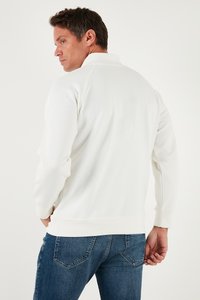 Valge fliisist pullover, millel on seisakrae ja pikad varrukad, sujuva tekstuuriga ja soonikkoes varrukatooted. Sobib siniste teksapükstega.