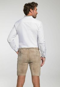 Weißes langärmliges Hemd kombiniert mit beigen Shorts. Die Shorts haben eine glatte Textur, Taschen und ein tailliertes Design.