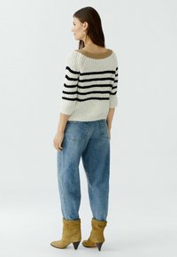 Pull en maille avec des rayures noires et blanches, manches courtes et un col beige. Assorti à un jean bleu ample et des bottines beiges.