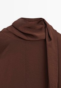 Bruin draperend stof met een gladde textuur, voorzien van een sjaalachtige halslijn en naadloze details. Subtiele glans versterkt de visuele diepte.