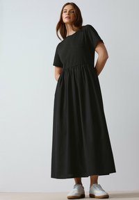 Vestido maxi negro hecho de una tela suave, con un cuerpo ajustado y cintura fruncida. Combinado con zapatillas blancas para un look casual.