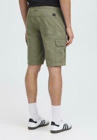 Bermudas cargo verde oliva con múltiples bolsillos laterales, hasta la rodilla, hechas de un tejido resistente. Combinadas con zapatillas blancas y calcetines cortos.