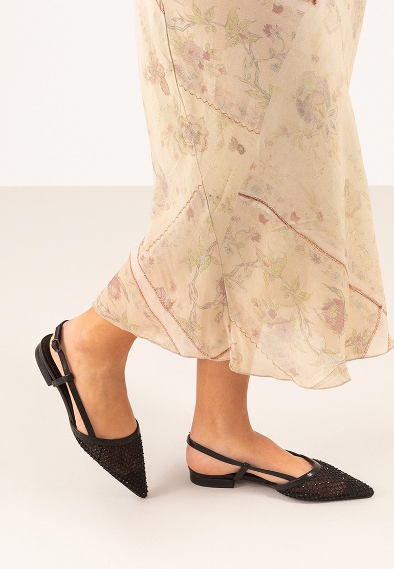 Zapatos negros de tipo slingback con punta afilada, con un diseño de malla tejida en la parte frontal, tacón plano y correa de tobillo ajustable.