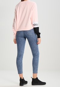 Sudadera corta de color rosa claro con mangas negras, que presenta letras blancas. Combinada con jeans ajustados azules y botas negras hasta el tobillo.