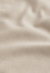 Texturierten Stoff in hellbeige mit einem subtilen geometrischen Muster, das feine gewebte Details und eine glatte Oberfläche aufweist.