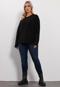 Czarny, oversize sweter wykonany z miękkiego dzianiny, sparowany z ciemnoniebieskimi skinny jeansami oraz czarnymi botkami za kostkę z grubą podeszwą.