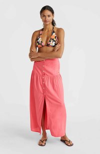 Haut de bikini noir à fleurs avec un décolleté halter associé à une jupe maxi corail avec des boutons sur le devant et une fente sur le côté, complété par des tongs noires.