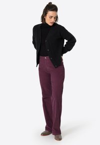 Schwarze Strickjacke mit einem strukturierten Muster, kombiniert mit locker sitzenden, dunkelvioletten Cordhosen. Braune Lederstiefeletten runden das Outfit ab.