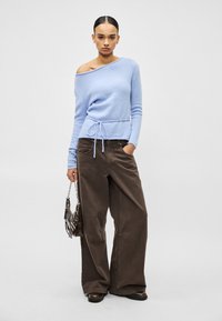 Pull bleu clair à épaules dénudées avec taille à cordon, associé à un pantalon large marron. Les tissus texturés créent un look décontracté avec une coupe ample.