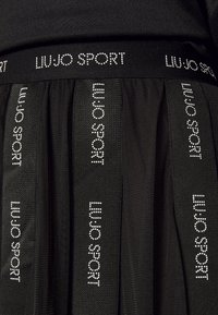 Czarna plisowana spódnica z pasem w talii ozdobionym napisem "LIUJO SPORT" z białych kryształków. Materiał ma gładką fakturę i sportowy design.