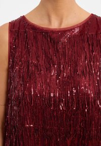Bordeaux mouwloze top met textuurfranjers van pailletten, die een glinsterend oppervlak creëren. Ronde halslijn met een gladde stofafwerking.