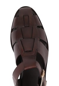 Brune lær herresandal med brede, vævede stropper og en gylden spænde, set ovenfra mod en hvid baggrund.