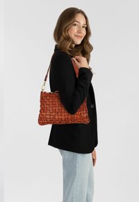Borsa in pelle intrecciata di un ricco marrone con chiusura a zip e tracolla removibile, caratterizzata da una forma rettangolare e superficie texturizzata.