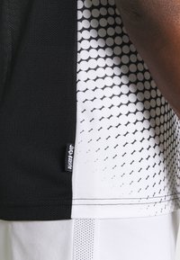 Czarna i biała sportowa koszulka z siateczkowego materiału, z wzorem w formie kropkowanego gradientu po jednej stronie oraz metką z logo na szwie.