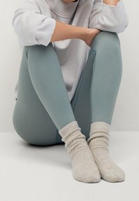 Persona sentada con las piernas cruzadas, usando leggings de canalé azul claro, calcetines de punto color crema y un suéter holgado gris claro.