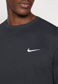 Μαύρο αθλητικό μακρυμάνικο μπλουζάκι από ελαφρύ ύφασμα, με λευκό λογότυπο Nike στην αριστερή πλευρά του στήθους. Λεία υφή και σχέδιο με στρογγυλή λαιμόκοψη.