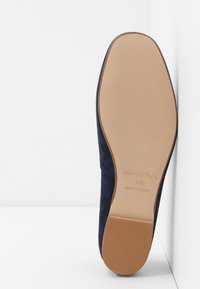 Chaussure à enfiler en suède marine avec une semelle lisse de couleur beige clair. Présente un logo en relief et un motif texturé pour une meilleure adhérence.