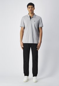 Hellgraues Poloshirt mit schwarzem Kragen und weißen Akzenten, kombiniert mit schwarzen Hosen und weißen Sneakers. Schlichte, legere Passform und Design.